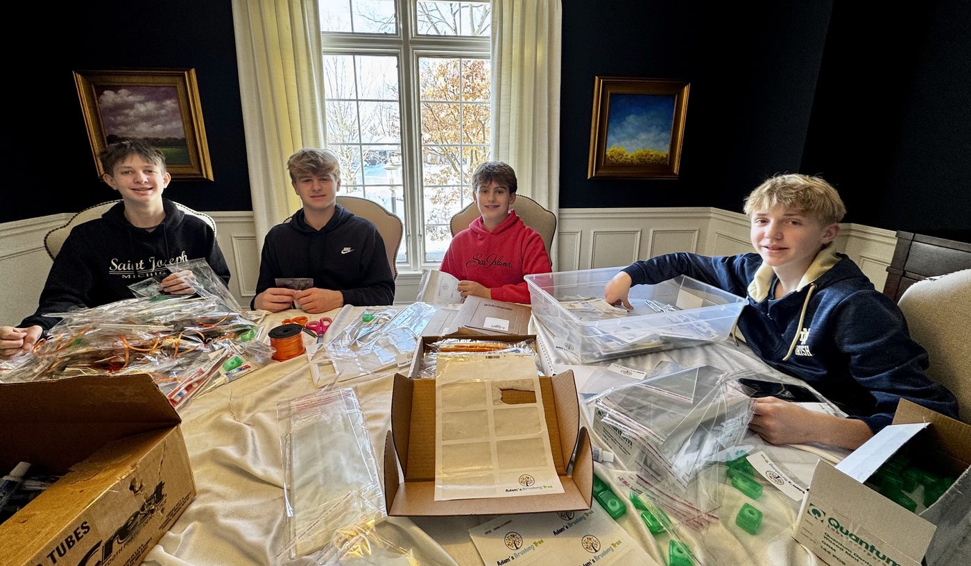 Four friends sitting around a table covered with clear bags, toothbrushes, toothpaste tubes, floss containers, ribbon and scissors, packing supplies into bags